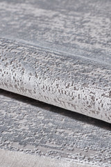 Close-up of the Radiant Edges Bordered Rug - Silver - M542B, showcasing its textured, metallic silver and gray surface with a shimmering pattern; rug is partially rolled to highlight its sheen and intricate design.