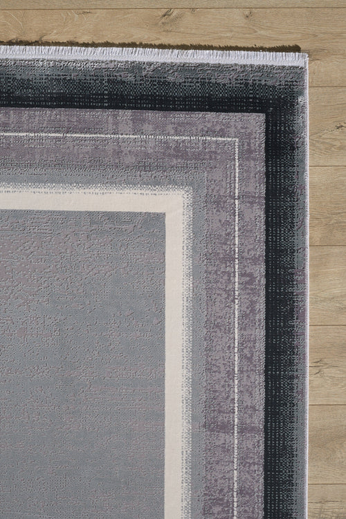 Load image 1 in gallery view. A close-up of the Radiant Edges Bordered Rug - Silver - M542B shows its rectangular, machine-made design with layered geometric borders in gray, purple, and white tones on a light wood floor.