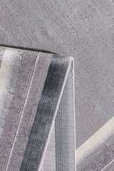 Close-up of the Radiant Edges Bordered Rug - Silver - M542B, featuring a folded, flat pile with textured horizontal stripes in grey, white, and muted blue tones against a matching textured grey background.