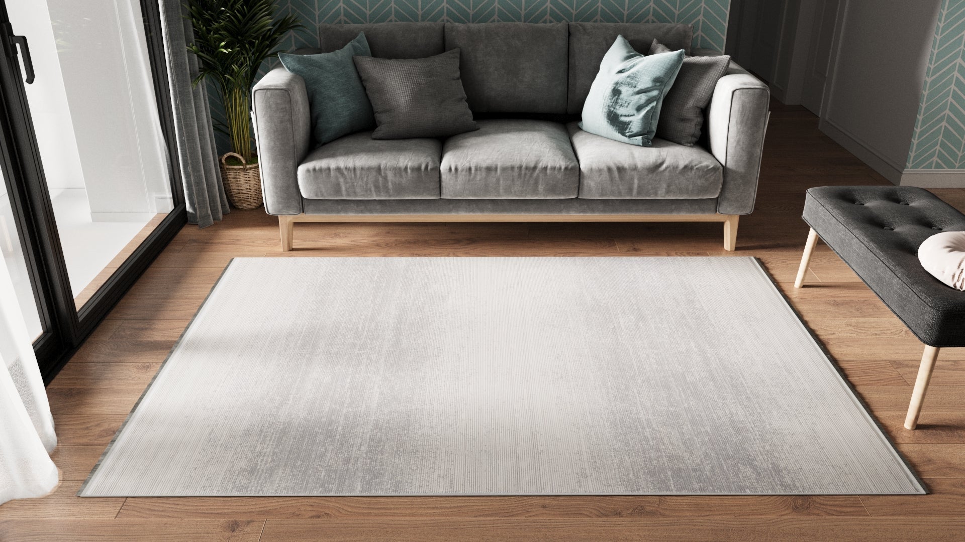 A modern living room with a light gray sofa, assorted pillows, the Radient Silver Haze Ombre Rug - M497D on wooden floor, a small upholstered bench, and a plant by a patterned teal wall. Natural light streams through large windows.