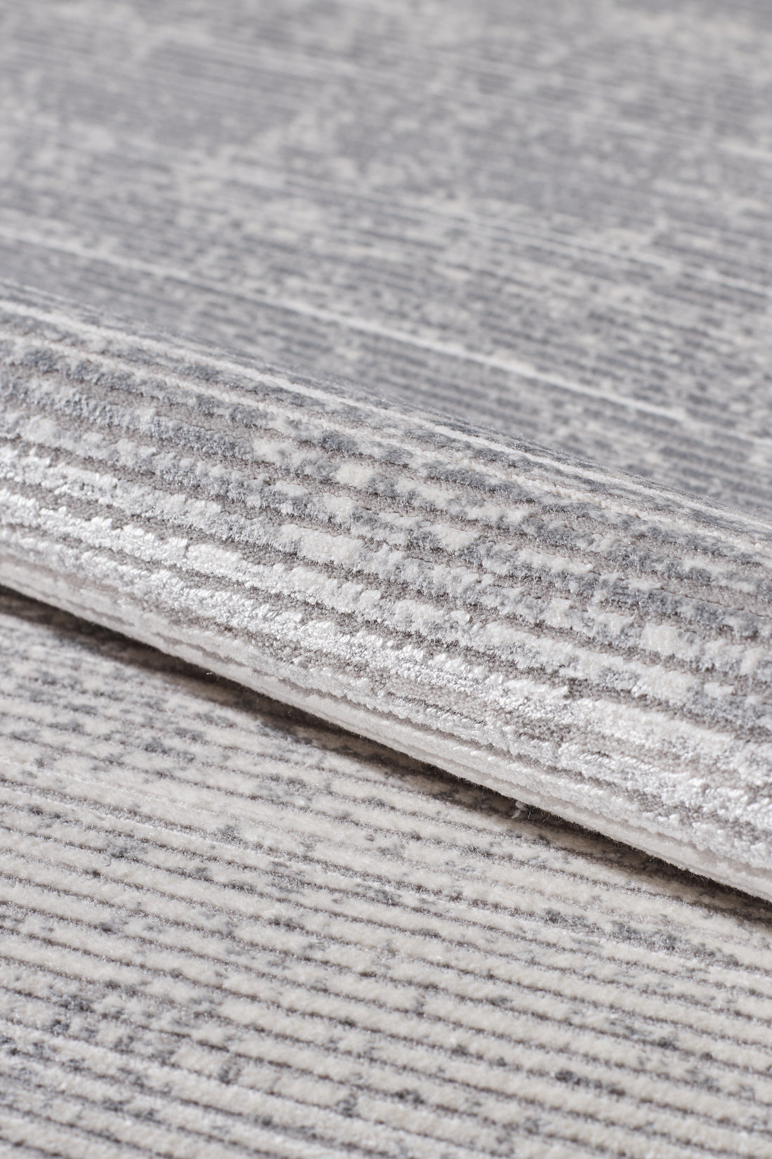 A close-up of the Radient Silver Haze Ombre Rug - M497D shows its soft, minimalist fabric in gray and white with subtle stripes, speckles, and slightly raised textured areas for added interest.