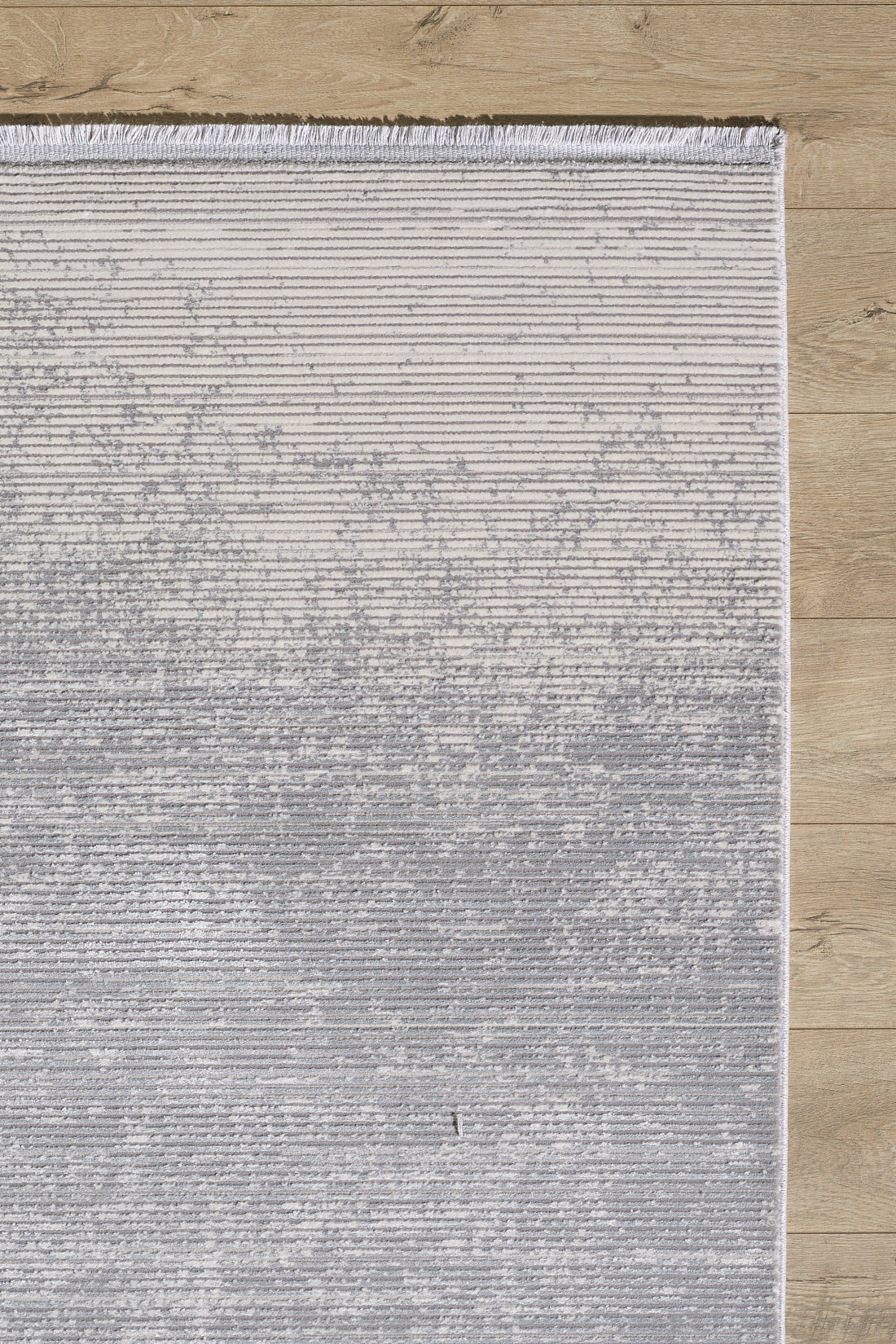 The Radient Silver Haze Ombre Rug - M497D is a rectangular, machine-made rug featuring a gradient from light to dark gray, subtle horizontal lines, and fringe on the top edge, shown on a light wood floor for a minimalist look.
