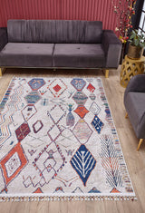 A modern living room with a gray velvet sofa, matching armchair, wood flooring, gold side table with a potted plant, red curtains, and the Rainbow Rhapsody - Washable Rug - JR5060 (Custom Size) featuring bold geometric designs.