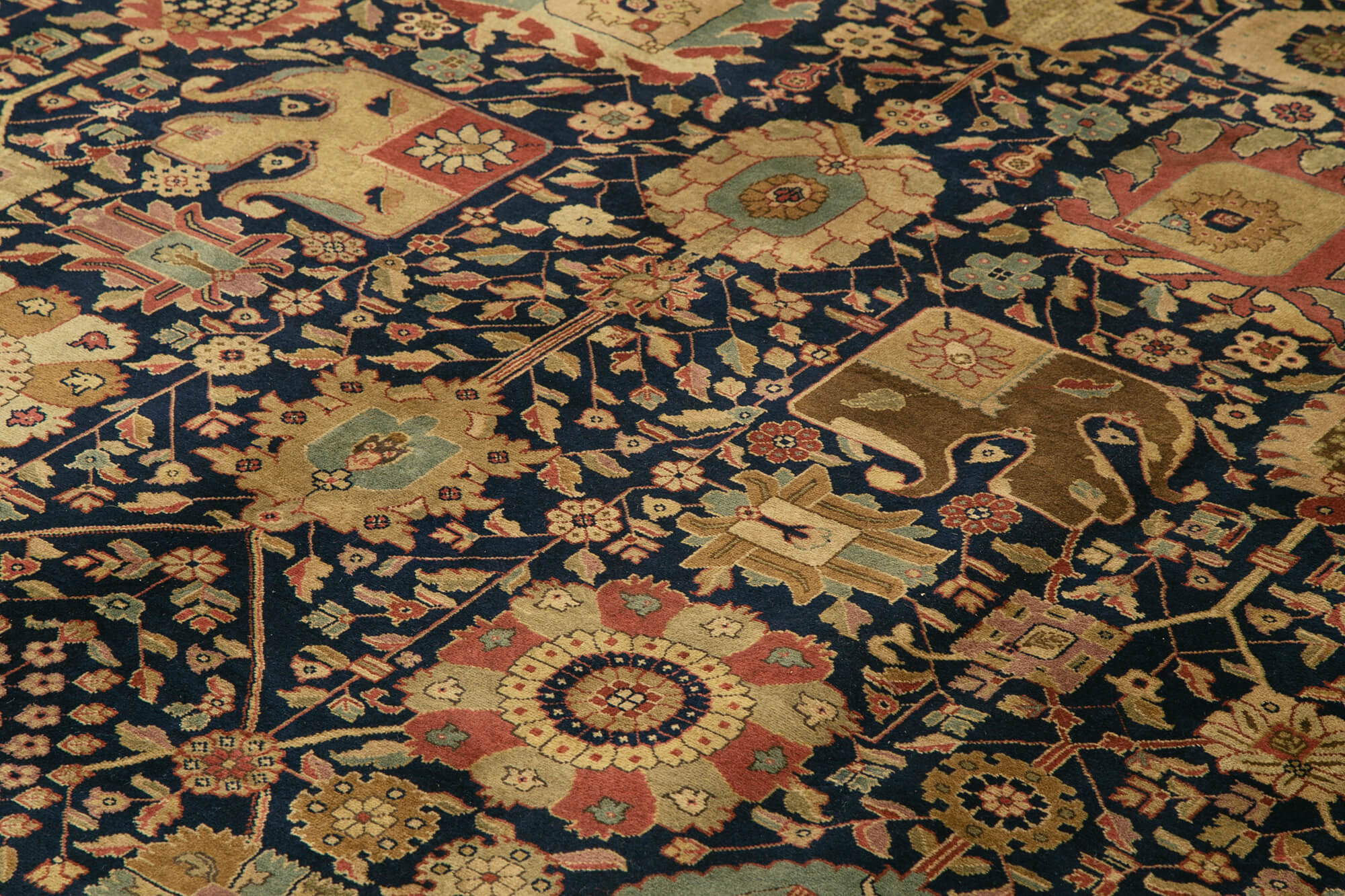 Detailed, ornate rug with intricate floral patterns and geometric shapes in shades of beige, gold, red, and blue on a dark background. The design features flowers, leaves, and stylized animal motifs.