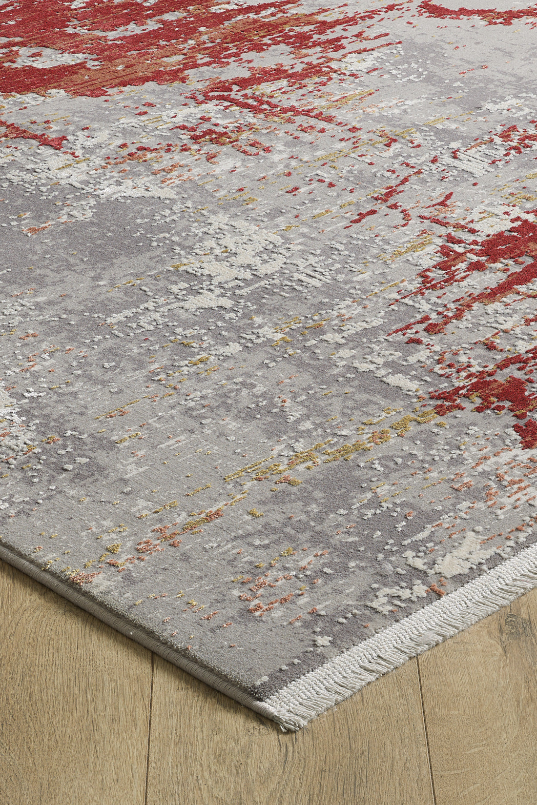 A close-up of the Red Strokes Premium Rug - 1052EB, a machine-made acrylic-viscose blend in gray, white, red, and yellow tones on a light wood floor; features a textured surface and finished edges with visible fibers.