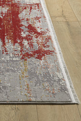 A close-up of the Red Strokes Premium Rug - 1052EB on a wooden floor, displaying an abstract rectangular design in red, gray, white, and yellow with fringe along the shorter edges.