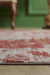 Close-up of the Red Strokes Premium Rug - 1052EB, featuring red and beige abstract patterns on a wooden floor, with a green wall and wooden chair softly blurred in the background.