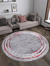 A modern living room with a gray sectional, throw pillows, a round side table, and the Refined and Timeless - Washable Rug - JR1500—gray center with red/white circles—on dark wood floors. Decor shelves line the back wall.