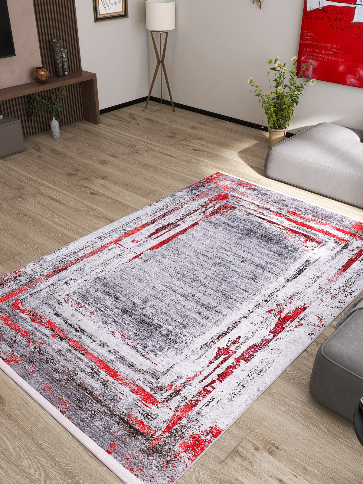 A modern living room with light wood flooring, gray furniture, and the Refined and Timeless - Washable Rug - JR1500 in abstract red, gray, and white—ideal for high-traffic, allergy-friendly spaces—plus a potted plant, floor lamp, and vibrant artwork.