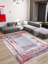 Modern living room with a grey L-shaped sofa, light wood floor, "Refined and Timeless - Washable Rug - JR1500 (Custom Size)" in red and grey—perfect for high-traffic areas—white walls with red and white art, large window, and dark curtains.