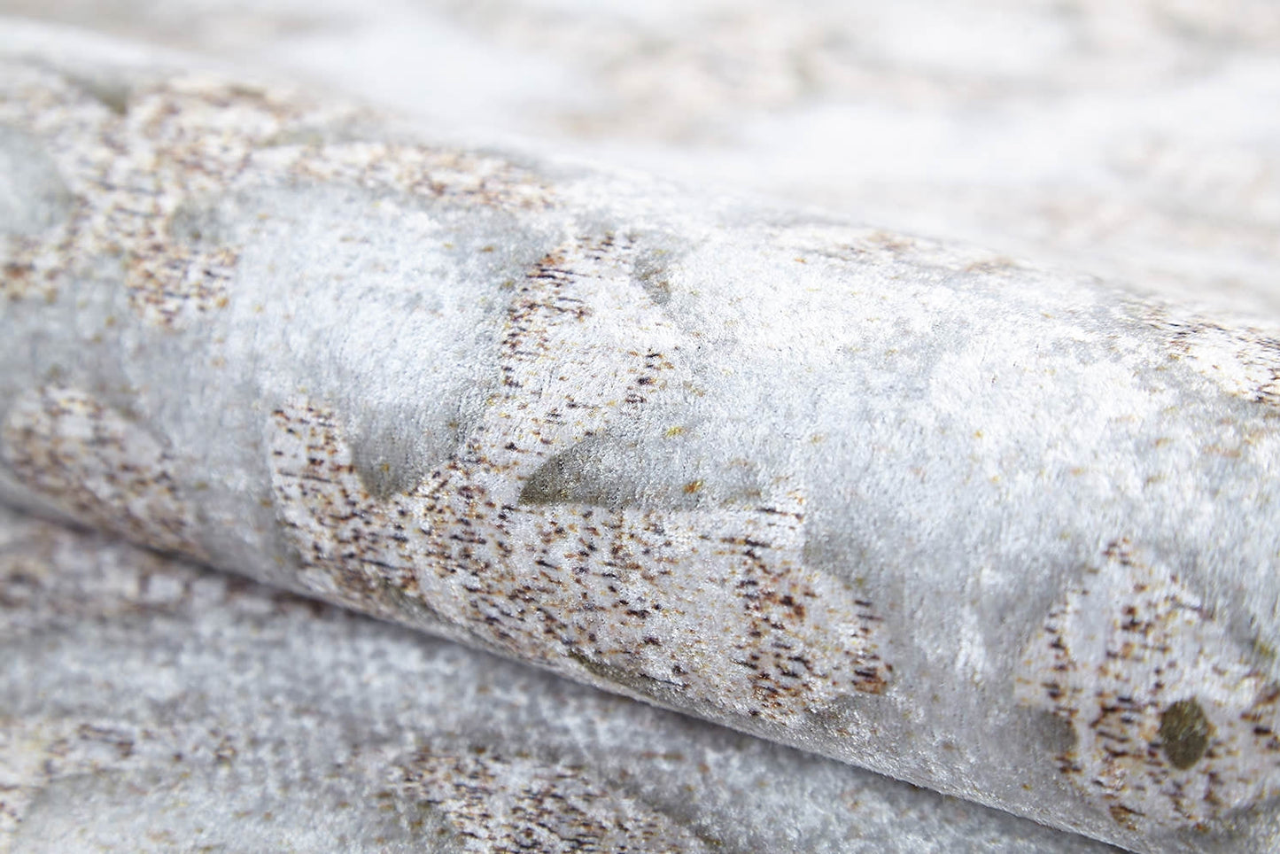 A close-up of the Regal Embellishment - Washable Rug - JR1590 (Custom Size) rolled up, featuring a soft, slightly fuzzy light grey and beige surface with abstract designs—ideal for high-traffic areas.