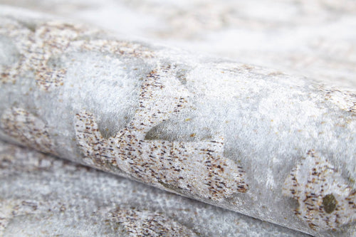 Load image 1 in gallery view. A close-up of the Regal Embellishment - Washable Rug - JR1590 (Custom Size) rolled up, featuring a soft, slightly fuzzy light grey and beige surface with abstract designs—ideal for high-traffic areas.