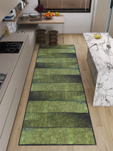 A modern kitchen with light wood floors, marble countertops, and a Regal Texture - Washable Rug - JRN34 (Custom Size) in green for high-traffic areas. Two wooden stools sit by the counter, while plants and fruit freshen up the space.