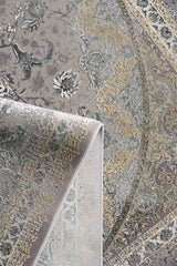 A close-up of the Reimagined Heritage Modernised Medallion Rug - Dust - M642B, featuring intricate floral and geometric patterns in gray, beige, gold, and cream with a folded corner revealing the underside, inspired by classic Turkish designs.
