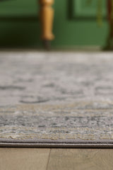 A close-up of the Reimagined Heritage Modernised Medallion Rug - Dust - M642B on a wooden floor, with a blurred green wall and wooden furniture leg in the background.