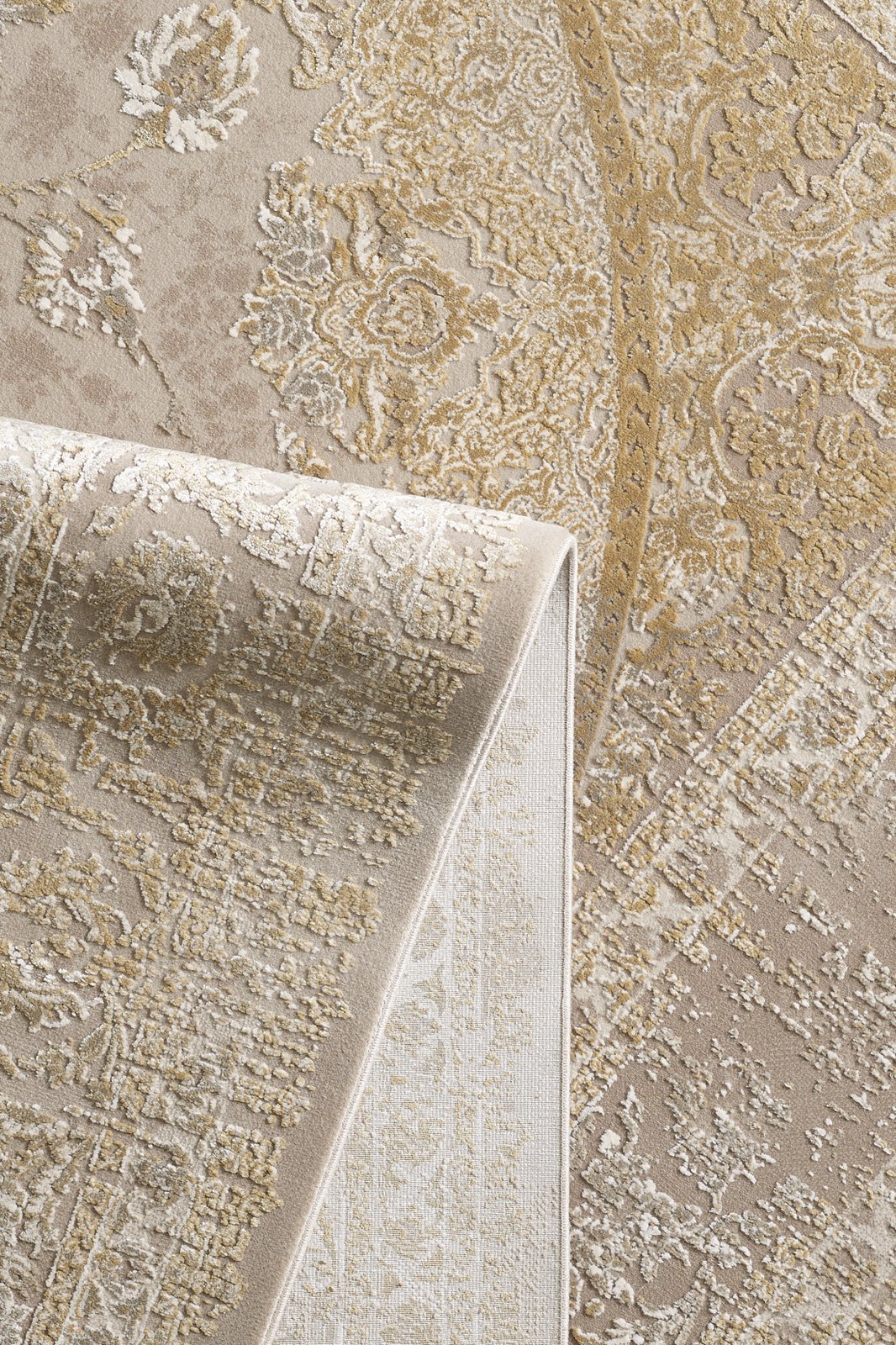 A close-up of the Reimagined Heritage Modernised Medallion Rug - Gold - M642F, featuring beige and gold tones, with a folded corner showcasing its detailed texture and intricate design on both sides.