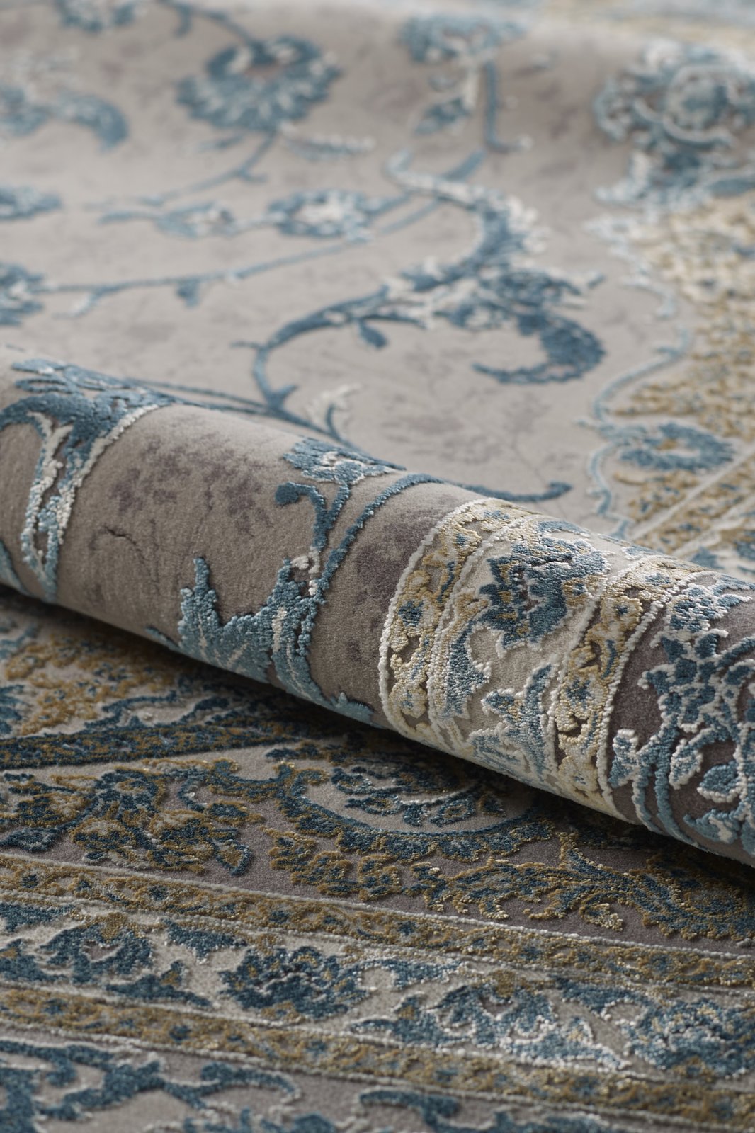 A close-up of the Reimagined Heritage Modernised Medallion Rug - Sky - M642A, rolled up to showcase its textured surface and intricate medallion pattern in blue, gray, and beige.
