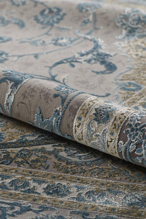 Load image 1 in gallery view. A close-up of the Reimagined Heritage Modernised Medallion Rug - Sky - M642A, rolled up to showcase its textured surface and intricate medallion pattern in blue, gray, and beige.