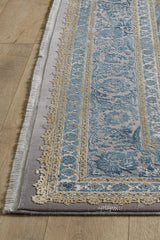 A close-up of the Reimagined Heritage Modernised Medallion Rug - Sky - M642A, featuring a blue and gold intricate pattern, light fringe, and grey border, displayed on a light wood floor.