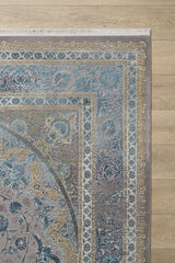 A close-up of the Reimagined Heritage Modernised Medallion Rug - Sky - M642A, featuring ornate blue, gold, and beige patterns with intricate borders and white fringe, displayed on a light wooden floor.