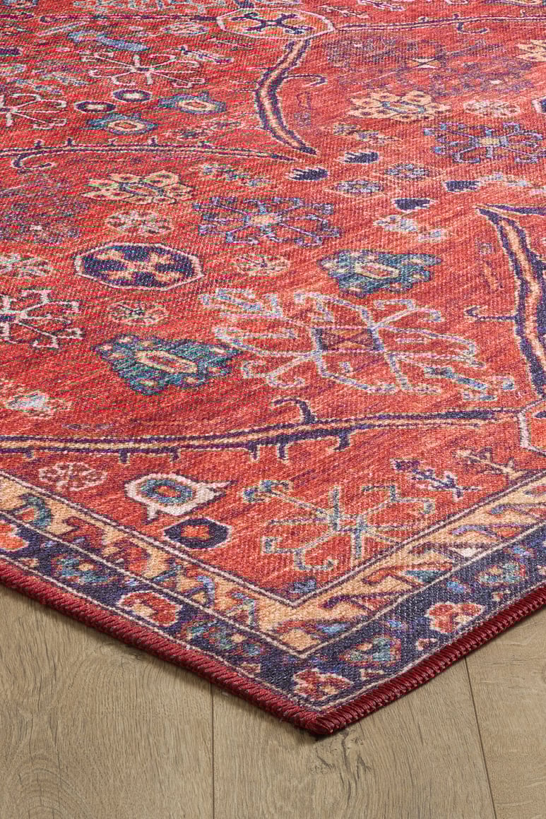 A close-up of the Rhapsody Authentic Red Washable Rug - LCC3033 (Outlet) US shows its detailed geometric and floral patterns in blue, beige, and green on a light wood floor—ideal for high-traffic areas.