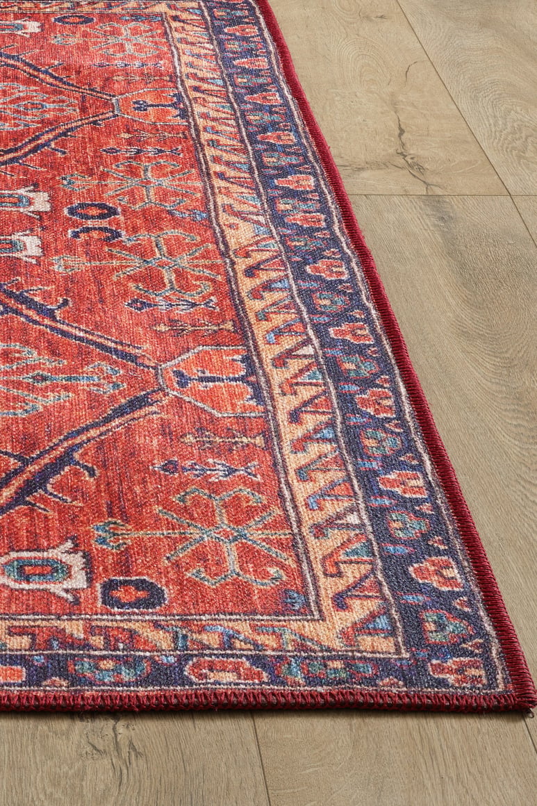 A close-up of the Rhapsody Authentic Red Washable Rug - LCC3033 (Custom Size) showcases its geometric motifs and detailed border on a light wood floor, highlighting its visible texture and durability for high-traffic areas.