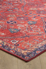 A close-up of the Rhapsody Authentic Red Washable Rug - LCC3033 (Custom Size), featuring intricate multicolor patterns and a geometric border on a light wood floor. Its visible corner highlights its durability, ideal for high-traffic areas.