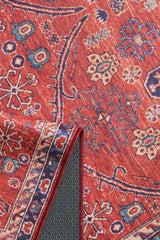 A close-up of the Rhapsody Authentic Red Washable Rug - LCC3033 (Custom Size) shows intricate blue, cream, and yellow floral and geometric patterns. A folded corner reveals a textured gray non-slip backing, perfect for high-traffic areas.