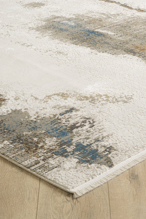 Load image 1 in gallery view. A close-up of the Riverstone Reflections Premium Area Rug - M685L, a modern machine-made acrylic-viscose rug with an abstract cream, blue, and brown design on a light wood floor. Features soft texture, finished edges, and short white fringe.