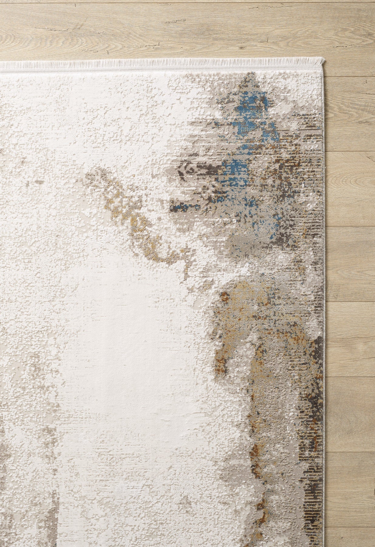The Riverstone Reflections Premium Area Rug - M685L showcases an abstract, distressed marble pattern in beige, gray, brown, and blue tones. Shown partially on a light wood floor.