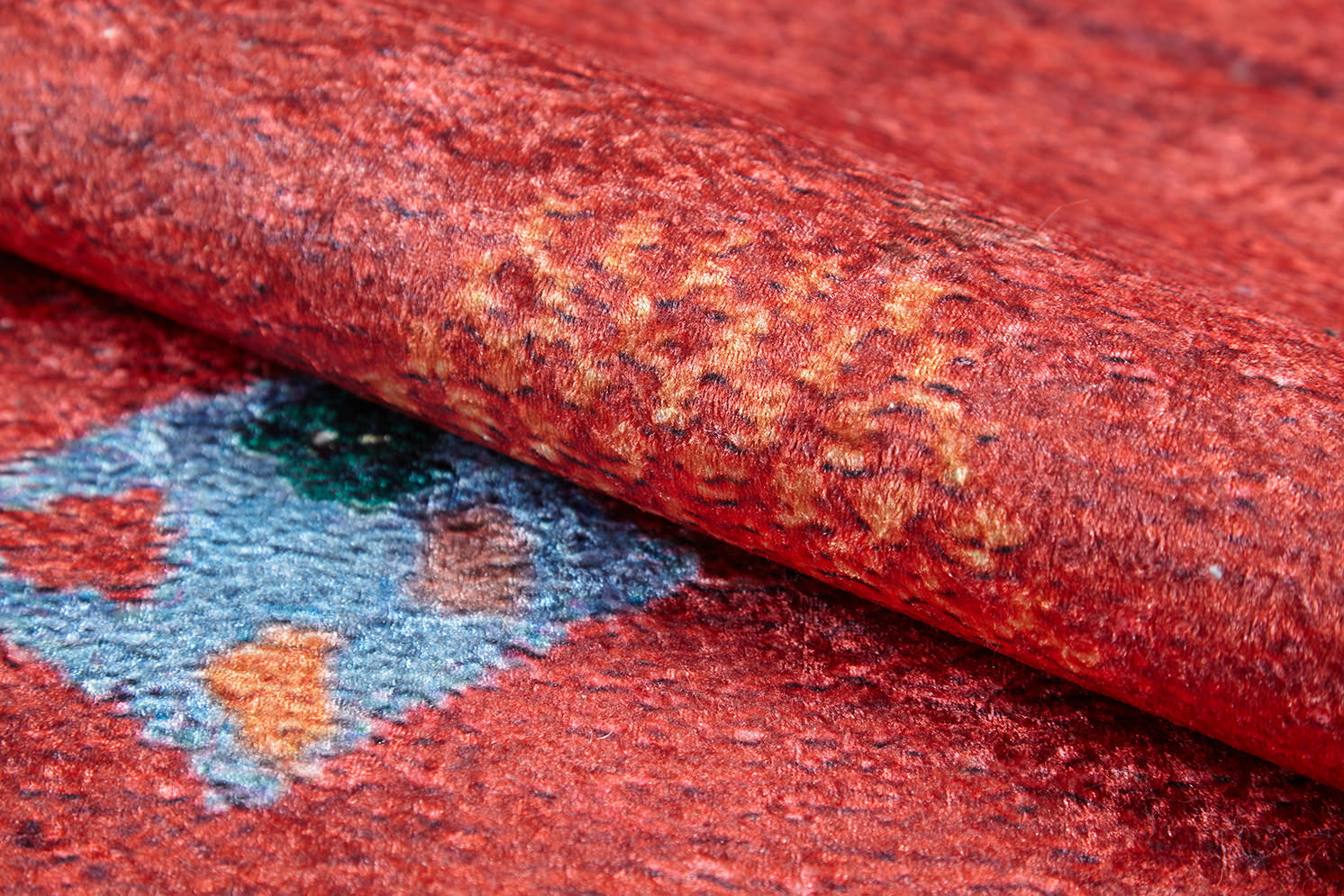 A close-up of the Rosy Blush Machine-Washable Rug (JRS5067) shows its red surface with a vibrant blue, green, orange, and yellow geometric pattern. The rug’s visible fibers and texture make it ideal for high-traffic spaces.