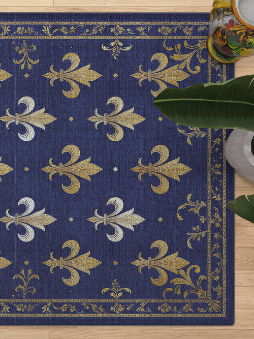 Load image 1 in gallery view. The Royal Fleur - Washable Rug - JRS016 features blue tones with gold and silver fleur-de-lis patterns and ornate borders, perfect for high-traffic areas. Styled on a light wood floor beside a leafy green plant and a small table.