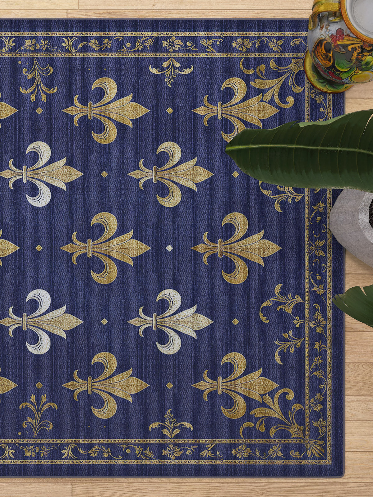 The Royal Fleur - Washable Rug - JRS016 (Custom Size) features a blue base with gold and silver fleur-de-lis and gold border details. Shown near a green plant and decorative object; perfect for high-traffic areas.