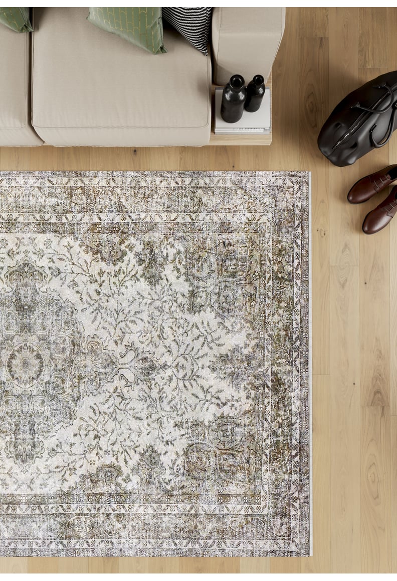 A top-down view of the Royal Legacy - Washable Rug - JR207, beige and patterned, on a light wood floor beside a beige sofa with pillows, books, boots, and a black bag—ideal for high-traffic areas.