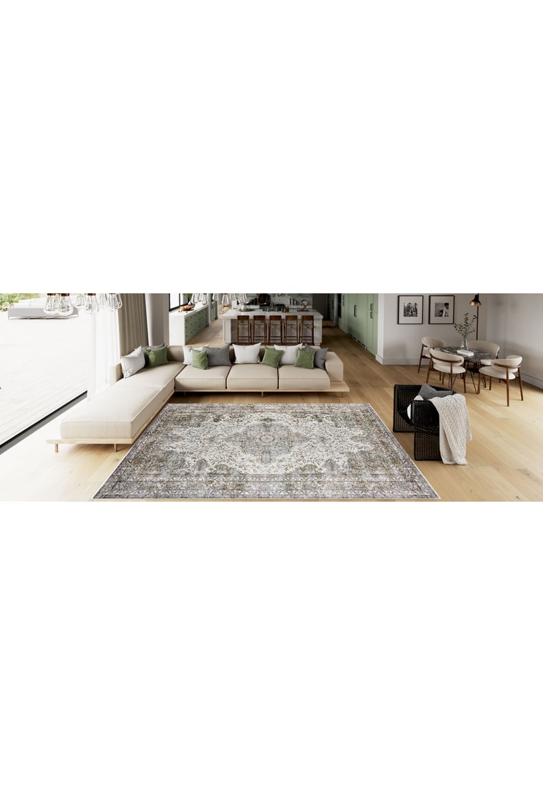 A spacious modern living room features the Royal Legacy - Washable Rug - JR207, ideal for high-traffic areas, on light wood floors with a beige sectional accented by green and gray pillows, a black side table, and an open dining area in the background.