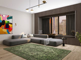 Modern living room with a large gray sectional, colorful abstract art, window seat with city view, minimalist neutral décor, and the Royal Vinework - Washable Rug - JRN1009 as a green area rug.