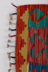 A close-up of the Royal Weft - Handwoven Kilim, showcasing colorful geometric patterns in red, orange, blue, and green wool with fringed tassels along the edge on a white background.