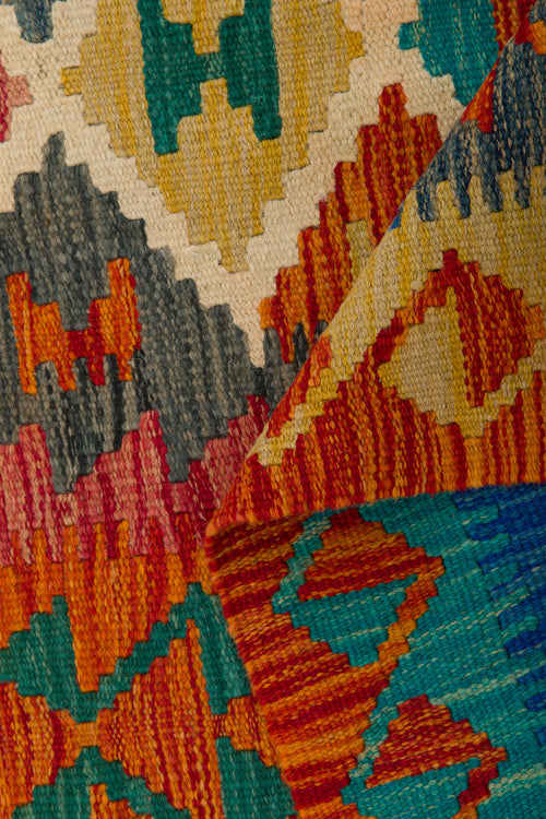Load image 1 in gallery view. The Royal Weft - Handwoven Kilim features colorful geometric patterns in red, blue, orange, yellow, and green. One corner is folded to reveal the reverse design. This flatweave rug showcases zigzags and diamond shapes.