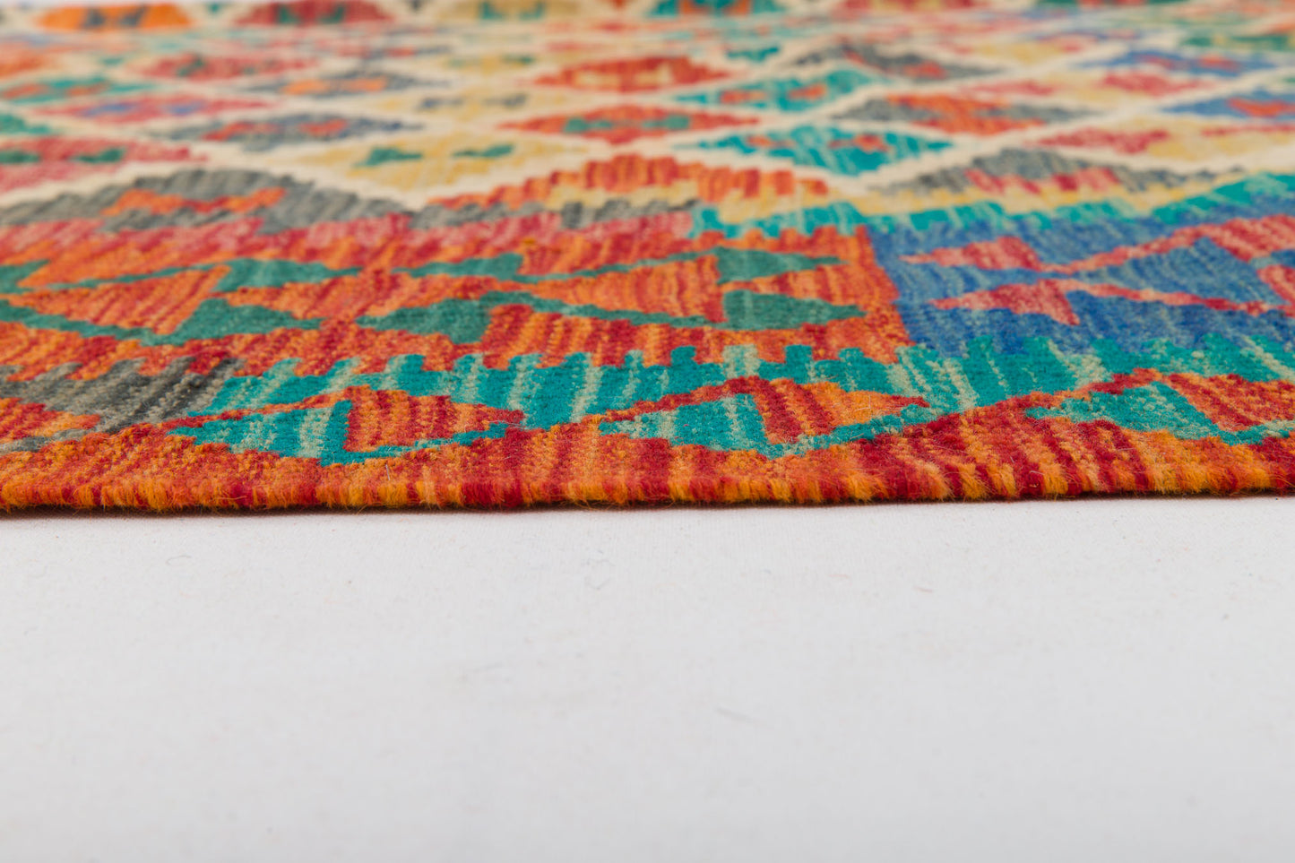 Close-up of the Royal Weft - Handwoven Kilim, showing its colorful geometric patterns in red, orange, yellow, blue, and green on a white floor. The image highlights the kilim’s edge and detailed weave texture.