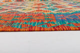 Close-up of the Royal Weft - Handwoven Kilim, showing its colorful geometric patterns in red, orange, yellow, blue, and green on a white floor. The image highlights the kilim’s edge and detailed weave texture.