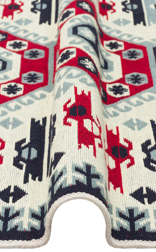 Load image 1 in gallery view. A close-up of the Ruby Weft - Washable Reversible Kilims - AR30 shows its geometric pattern in red, navy blue, and light grey on a cream background. The wavy draping highlights the intricate design and texture of this washable rug.