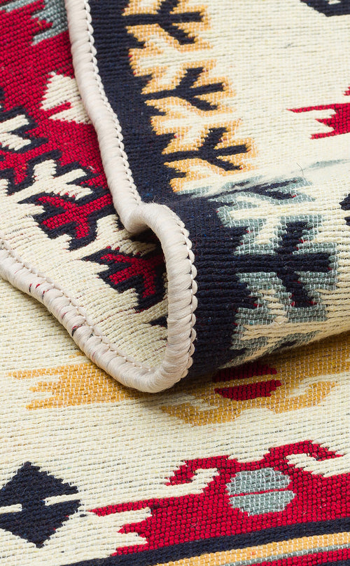 Load image 1 in gallery view. A close-up of Ruby Weft - Washable Double-Sided Kilims - AR30, partially folded to showcase its detailed stitching and bold geometric patterns in red, yellow, black, and ivory along the edge.