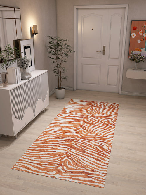 Load image 1 in gallery view. A hallway with light wood floors features the Rustic Mirage - Washable Rug - JRN40 (Custom Size) in an orange and white zebra print—perfect for high-traffic areas—plus a white sideboard, decor, potted plant, wall art, and a white door at the end.