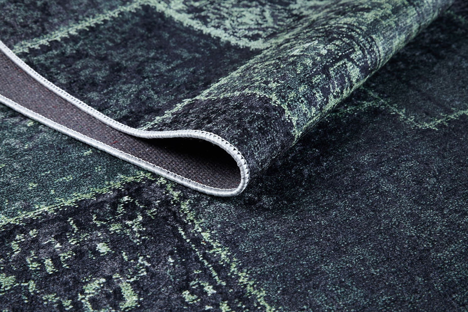A close-up of the Rustic Remix - Washable Rug - JR1710 (Custom Size) in dark green and black, featuring a lifted corner to reveal its textured underside and neat stitching—ideal for high-traffic areas.