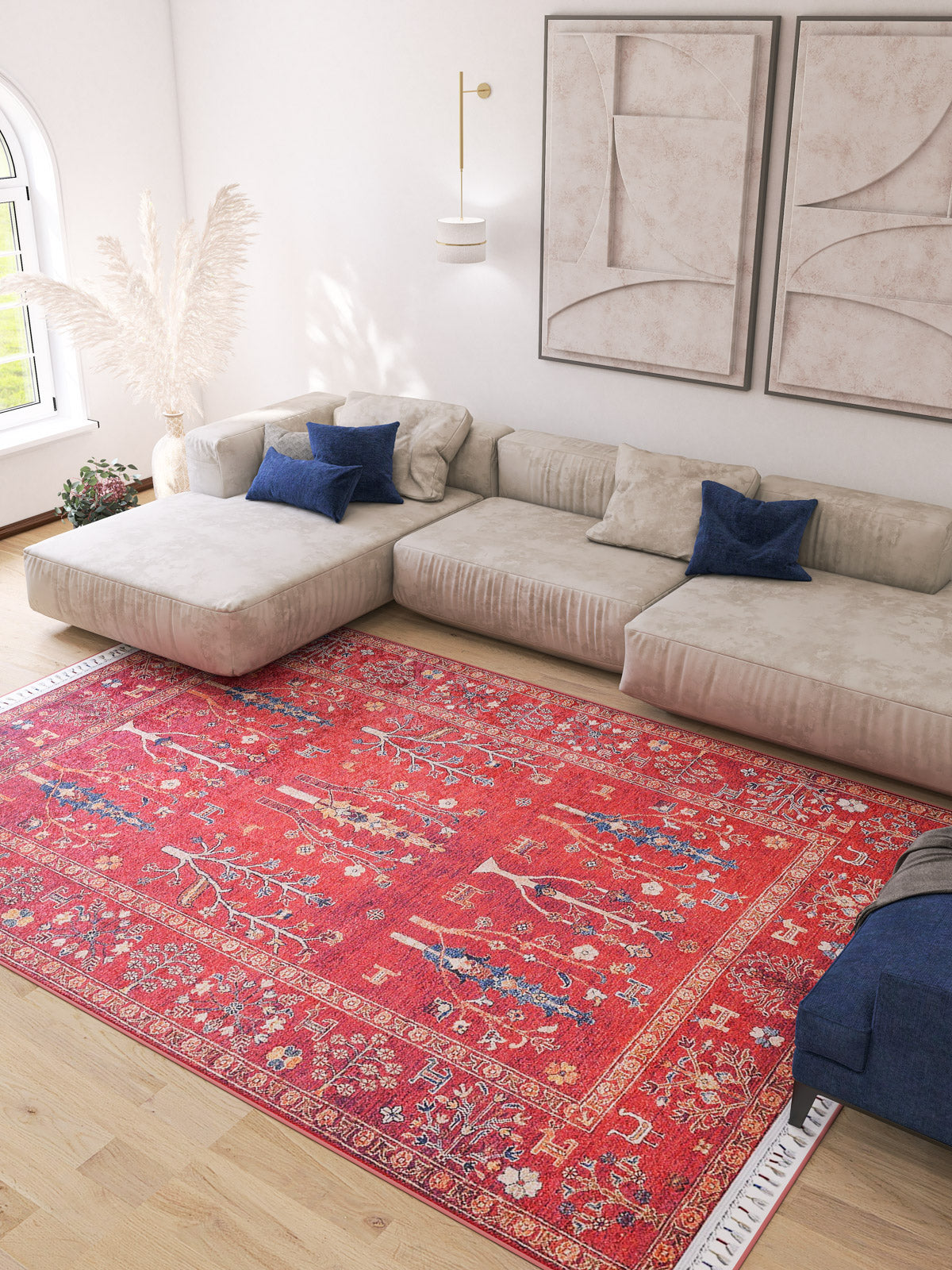 A modern living room with a large beige sectional, blue pillows, abstract wall art, and the vibrant Rustic Retreat - Washable Rug - JR5095 (Custom Size), perfect for high-traffic areas, plus natural light and pampas grass in the corner.