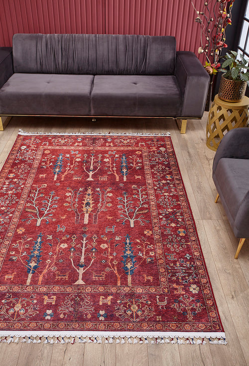 Load image 1 in gallery view. A living room features a dark gray sofa, matching armchair, and the Rustic Retreat - Washable Rug - JR5095 (Custom Size), with tree and animal designs—ideal for high-traffic areas. A plant in a stand sits by the sofa against a red-striped wall on light wood floors.