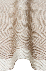 A close-up of the Sand Drift - Kilim - MNO02 beige flatwoven polyester rug, featuring a raised wavy fold running vertically through the center, highlights the fabric’s unique texture and pattern.