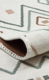 A close-up of the Sand Horizon - Washable Double-Sided Kilims - AR05 shows its cream base with green and brown geometric patterns, stitched edging, and a glimpse of the reversible underside.