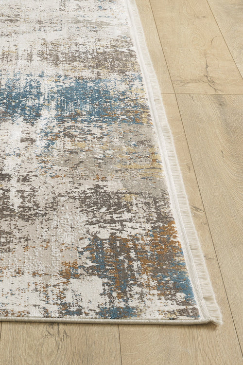 Load image 1 in gallery view. A close-up of the Sandy Papyrus Canvas Area Rug - M679L, a modern machine-made abstract design in blue, gray, white, and gold tones with fringed edges on the sides, displayed on a light wooden floor.