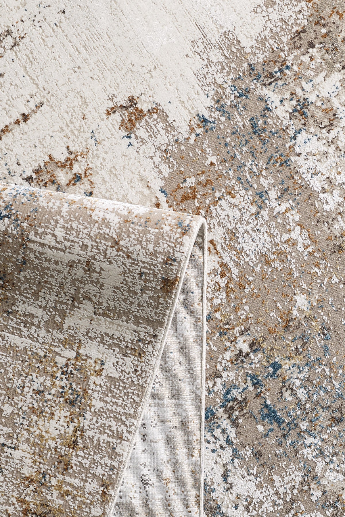 A close-up of the Sandy Papyrus Canvas Area Rug - M679L features abstract designs in beige, brown, white, and blue. A corner is folded over to showcase the rug's machine-made texture and thickness.